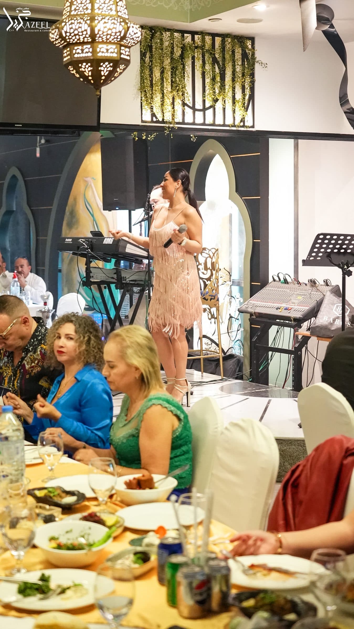 A singer on the stage during a celebration, with guests seated at the tables